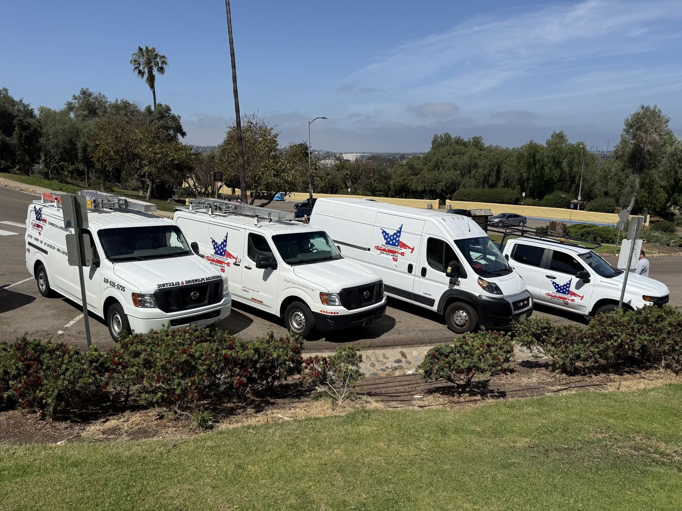 Four white American Construction work vehicles parked together on a hillside in San Diego, each carrying the company's star decal.