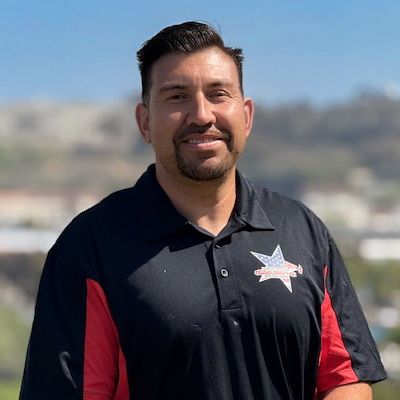 A man in a black and red work polo, photographed outdoors.