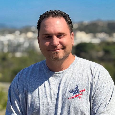 A man in a grey work shirt, photographed outdoors.