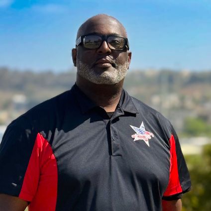 A man in a black and red work polo, photographed outdoors.