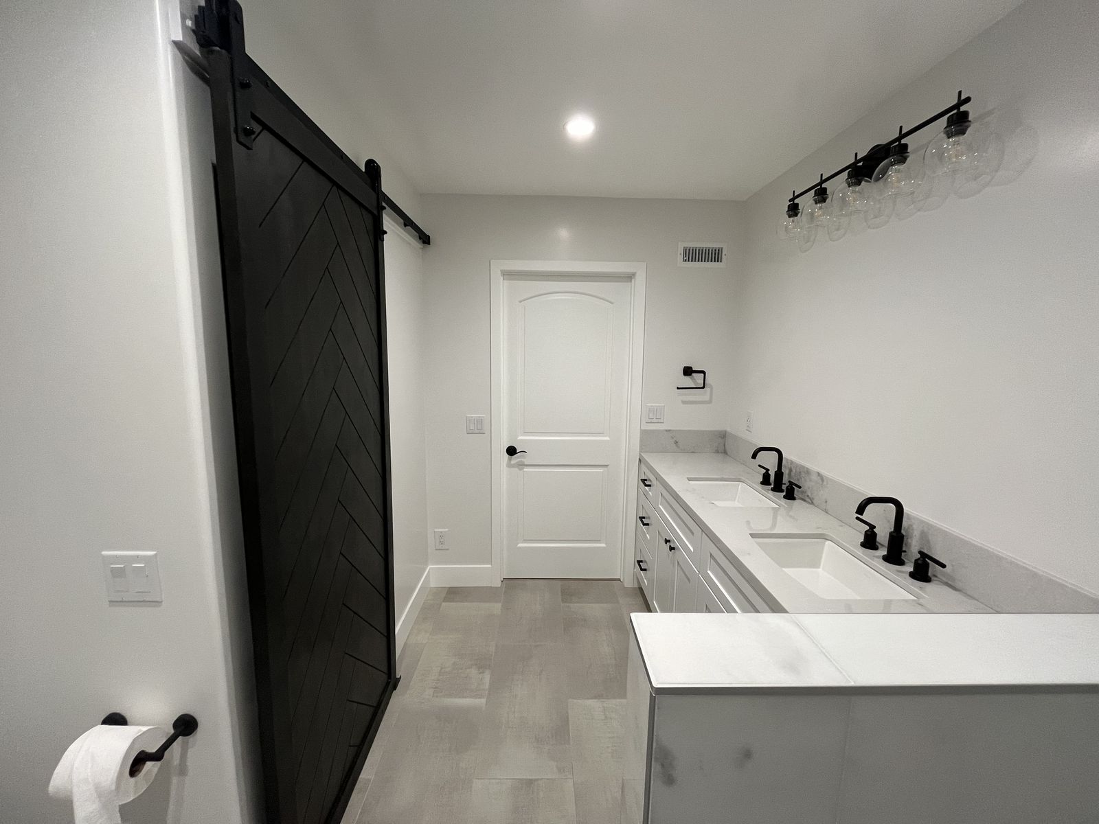 A finished bathroom with a double vanity, a sliding barn door and tile flooring.