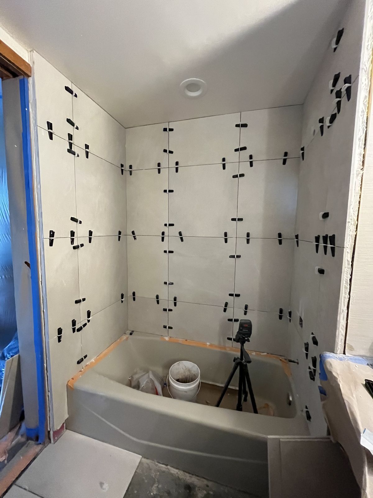 A bathtub surround mid-installation, with tile set on the walls and levelling clips still in place.