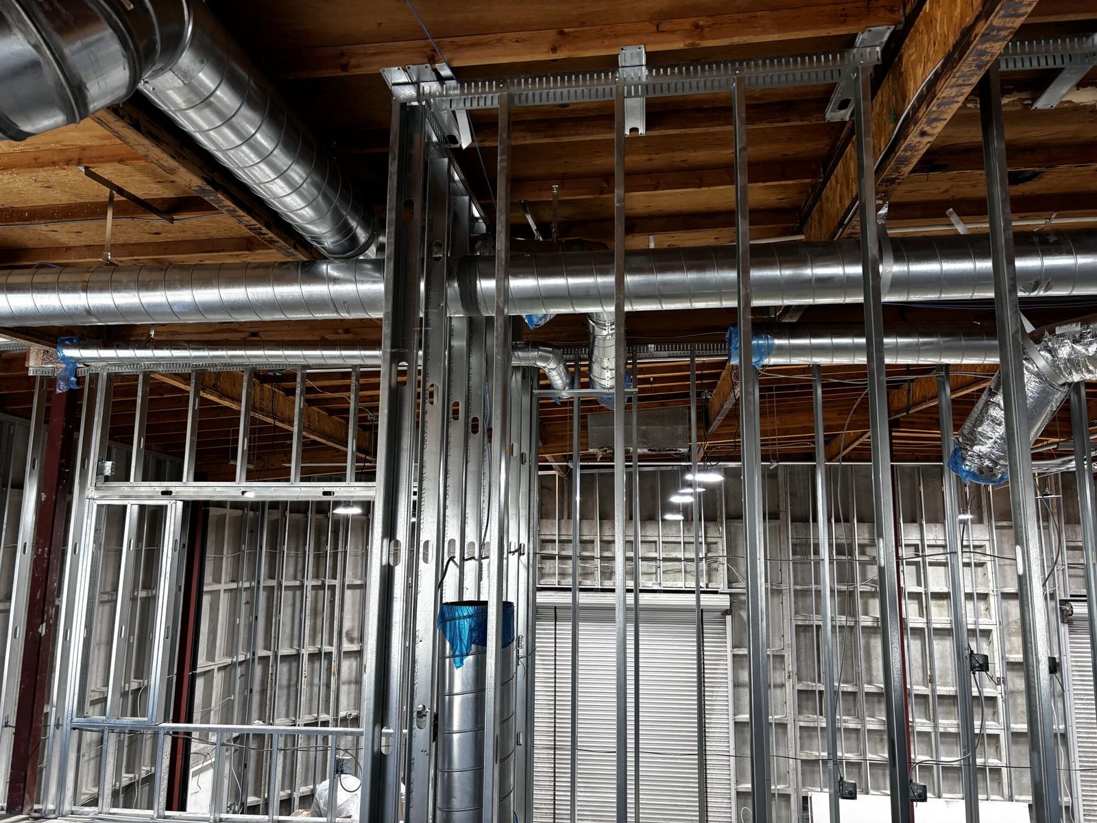 Sheet metal ductwork running above steel stud framing in an open commercial ceiling.