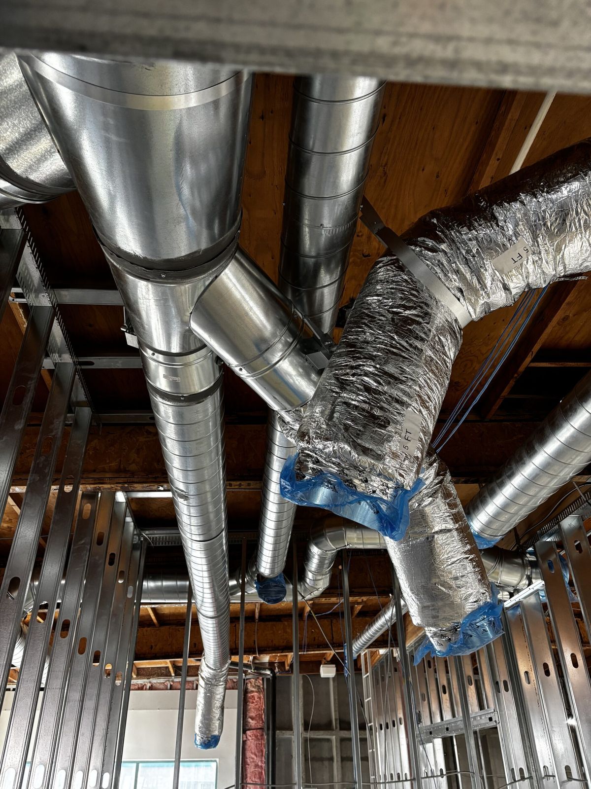 A spiral duct splitting into insulated flexible runs at a ceiling junction.