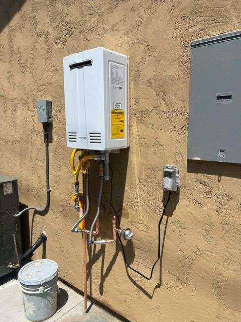 A tankless water heater mounted on an exterior stucco wall beside an electrical panel.
