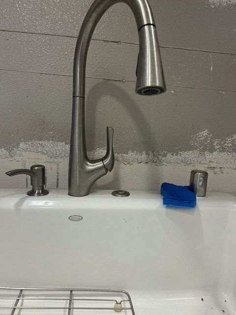 A new pull-down kitchen faucet and sink installed against a bare wall.