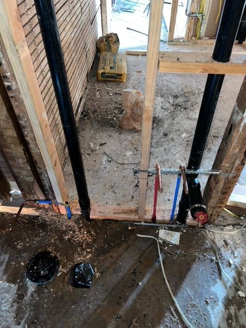 Black drain and vent piping run through open floor and wall framing.